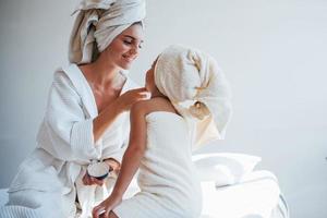 Using cream to clear skin. Young mother with her daugher have beauty day indoors in white room photo