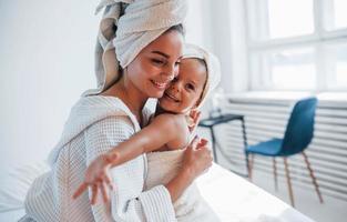 Young mother with her daugher have beauty day indoors in white room photo