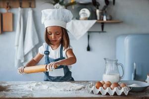 Cute kid in white chef uniform preparing food on the kitchen photo