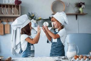 divertirse durante el proceso. niños de familia con uniforme de chef blanco preparando comida en la cocina foto