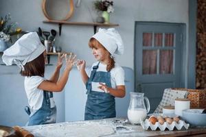 Having fun during the process. Family kids in white chef uniform preparing food on the kitchen photo