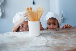 divirtiéndose con espaguetis. niños de familia con uniforme de chef blanco preparando comida en la cocina foto