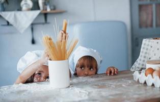 Having fun with spaghetti. Family kids in white chef uniform preparing food on the kitchen photo