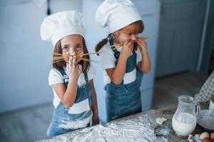 divirtiéndose con espaguetis. niños de familia con uniforme de chef blanco preparando comida en la cocina foto