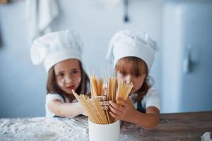 divirtiéndose con espaguetis. niños de familia con uniforme de chef blanco preparando comida en la cocina foto