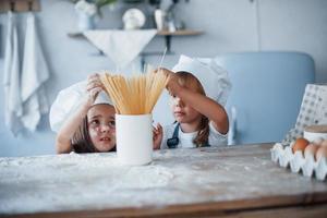 Having fun with spaghetti. Family kids in white chef uniform preparing food on the kitchen photo