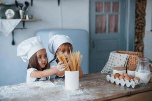 Having fun with spaghetti. Family kids in white chef uniform preparing food on the kitchen photo