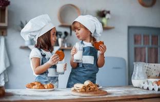 con vasos con leche. niños de familia con uniforme de chef blanco preparando comida en la cocina foto