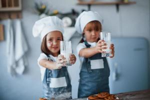 con vasos con leche. niños de familia con uniforme de chef blanco preparando comida en la cocina foto