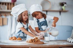 las galletas están listas. niños de familia con uniforme de chef blanco preparando comida en la cocina foto
