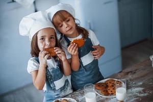 Positive mood. Family kids in white chef uniform eating food on the kitchen photo