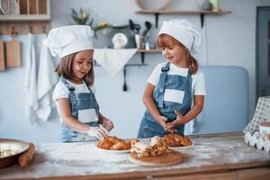 las galletas están listas. niños de familia con uniforme de chef blanco preparando comida en la cocina foto