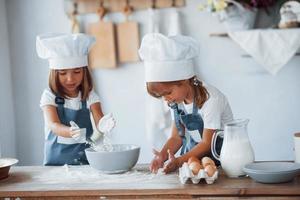 niños de familia con uniforme de chef blanco preparando comida en la cocina foto