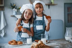 Positive mood. Family kids in white chef uniform eating food on the kitchen photo