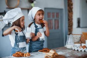 Wth glasses with milk. Family kids in white chef uniform preparing food on the kitchen photo