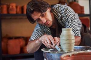 Makes lines with tool. Ceramist uses potter's wheel and creates a handmade clay product photo