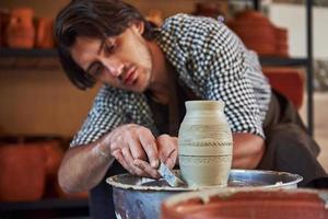 Makes lines with tool. Ceramist uses potter's wheel and creates a handmade clay product photo