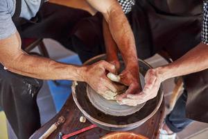 Close up view. Master teaches student. Two ceramist uses potter's wheel to create a handmade clay product photo