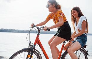 Two female friends on the bike have fun at beach near the lake photo