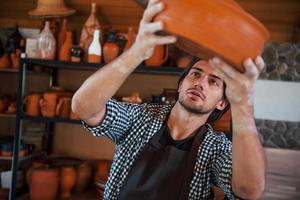 Young ceramist holds fresh handmade product made of clay in hands and looks at results of his work photo