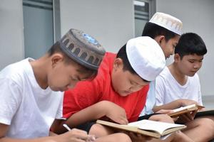 Asian muslim or islamic boys sitting with muslim boys in a row to pray or to do the religious activity, soft and selective focus. photo