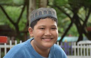 retrata a un niño musulmán o islámico asiático sentado en el parque escolar y sonriendo alegremente, con un enfoque suave y selectivo. foto