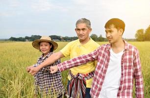 Portrait asian elderly man in yellow shirt is taking note planting information by asking and interviewing young asian man and female farmer nearby, soft and selective focus. photo