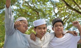 Young asian muslim boys raised hands, smilling and hugging each other to present happiness under the trees in the park, soft and selective focus. photo