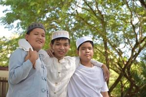 Young asian muslim boys raised hands, smilling and hugging each other to present happiness under the trees in the park, soft and selective focus. photo