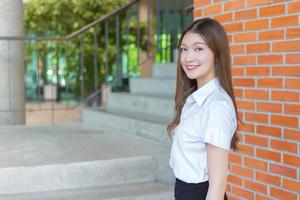 una hermosa joven estudiante asiática sonríe confiada y mira la cámara en el fondo de la universidad. foto