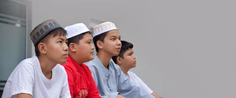 Asian muslim or islamic boys sitting with muslim boys in a row to pray or to do the religious activity, soft and selective focus. photo