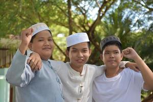 Young asian muslim boys raised hands, smilling and hugging each other to present happiness under the trees in the park, soft and selective focus. photo