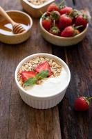 Strawberry yogurt in a wooden bowl with granola, honey, mint and fresh strawberry on  wooden background. Health food concept.