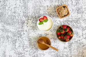 Top view of Strawberry yogurt in a wooden bowl with granola, honey, mint and fresh strawberry on wooden background. Health food concept. photo