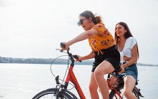 Two female friends on the bike have fun at beach near the lake