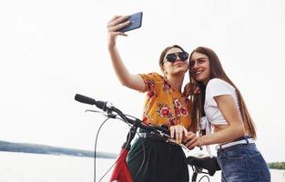 Making a selfie. Two female friends on the bike have fun at beach near the lake photo