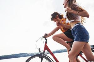 dos amigas en bicicleta se divierten en la playa cerca del lago foto