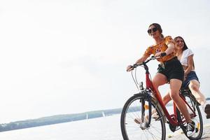 dos amigas en bicicleta se divierten en la playa cerca del lago foto