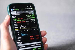 Businessman use smartphone in hand trading online stock exchange market charts graph board data investment economic on mobile screen Set index thai stock market Bangkok, Thailand - November 2022 photo