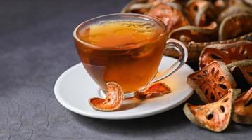 té de bael en vidrio con rodajas de bael secas sobre fondo de madera, jugo de bael - té de frutas de bael seco para la salud - aegle marmelos foto