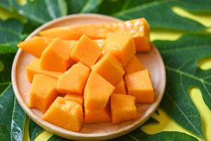 frutas de papaya sobre fondo de madera, rodajas de papaya maduras frescas en un plato de frutas tropicales con semillas de papaya y hojas de árbol de papaya