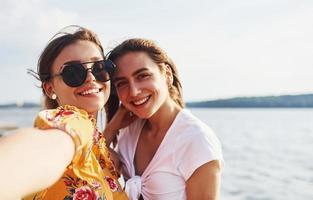 Selfie of two smiling girls outdoors that have a good weekend together at sunny day against the lake photo