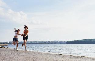 Two female friends runs and have fun at beach near the lake at sunny daytime photo