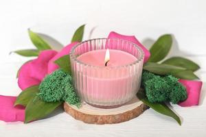 pink soy wax candle burning on a wooden saw cut podium with floral decor. Valentines day decoration for a holiday table set. photo