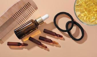 Hair growth ampules and serum solution next to omega 3 capsules and wooden comb on beige background. hair care medical treatment . top view photo