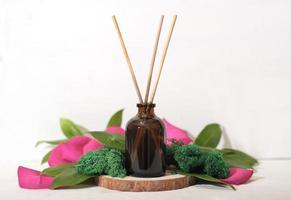 home scent, reed diffuser on wooden podium with green leaves and petals decor. floral fragrance for house ambience. photo