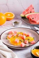 Fruit salad of watermelon, orange and pumpkin seeds on a plate on the table. Healthy food. Vertical