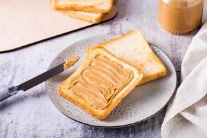 Bread toast with peanut butter on a plate and a jar of butter on the table photo