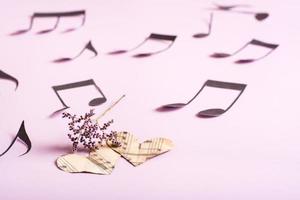 The concept of love for music. Two paper hearts, dry flowers and notes around on a pink background