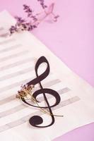 Paper musical clef on a sheet of music and dried flowers. Vertical view.